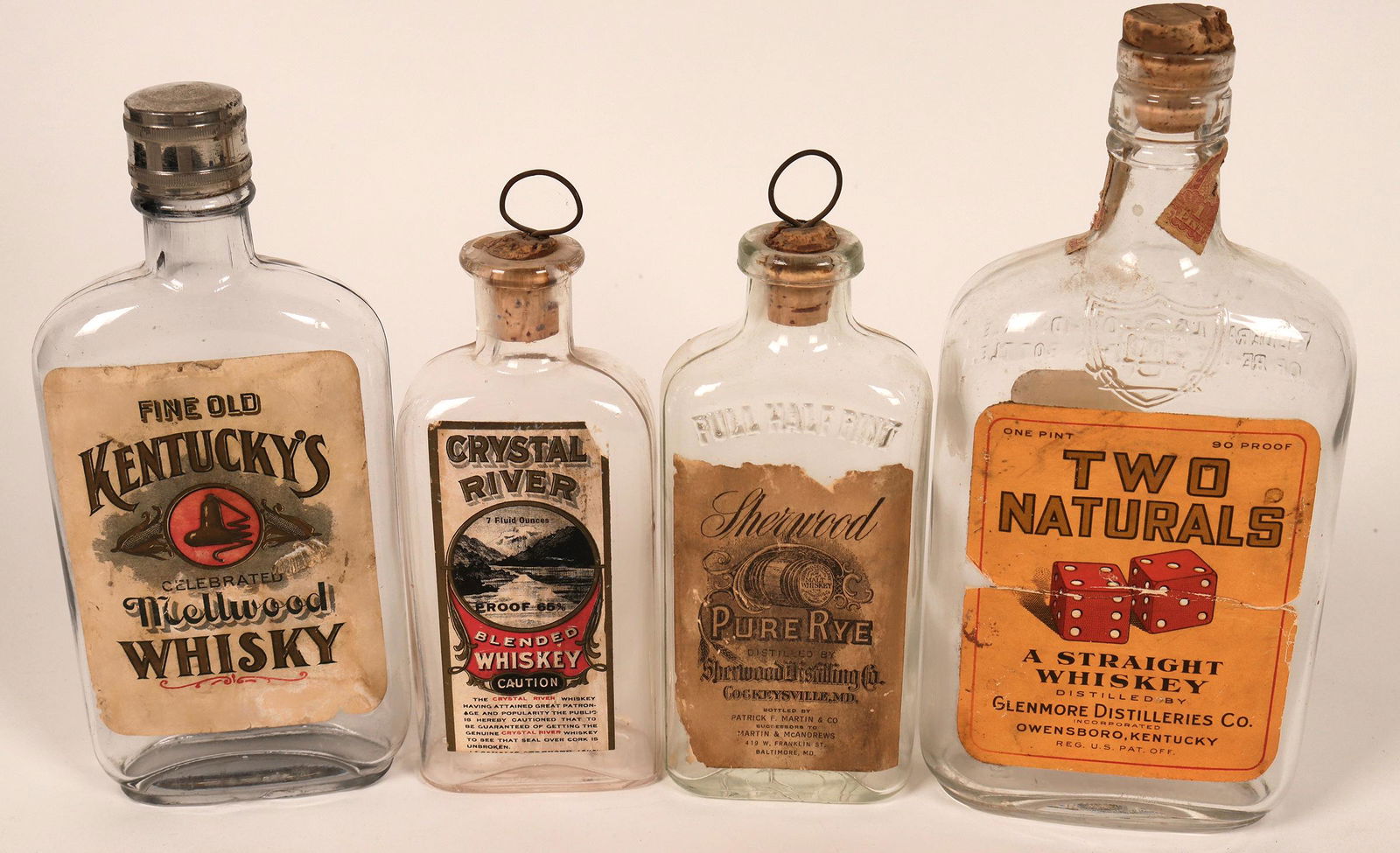 Early Whiskey Bottle Quartet (122775): Clear whiskey bottles from early 1900's.Included in the group of four clear glass, paper labeled bottles, is a Sherwood Pure Rye, Kentucky's Mellwood Whisky, Two Naturals Straight Whiskey and Crystal