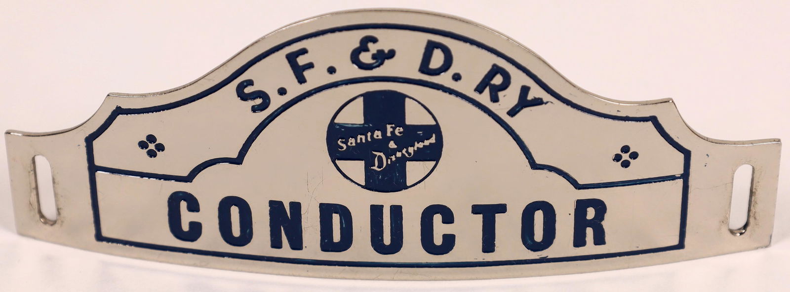 Santa Fe & Disney Railway Conductor Hat Badge (126644): Conductor Hat Badge for the Santa Fe & Disney Railway. Highly polished, silver-toned (nickel?) with black enamel lettering. No reverse stamp. Approx. 4 x 1-5/8 inches.Date: Country (if not USA): State