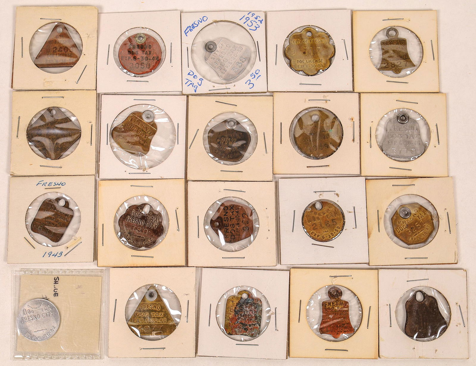 Fresno City Dog Tag Collection (120319): Twenty City of Fresno dog licenses, with most engraved "Dog Tax." Years include: 1940, 1942, 1943-1959. Most are brass, some aluminum. Shapes include: bell, triangle, round, scalloped, octagon, diamon