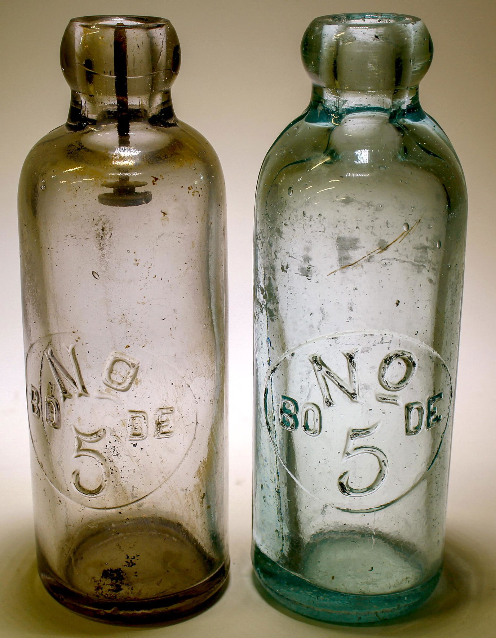 Soda Bottles / Bode No. 5/ 2 Items (89537): Item # 1 of 2: Embossed on the front of the bottles in a round slug plate are : No/ ( cu )/ BO....DE / 5 // Clear, Hutchinson style , soda bottle. 7" tall, squat top, tooled lip. Fairly clean with no