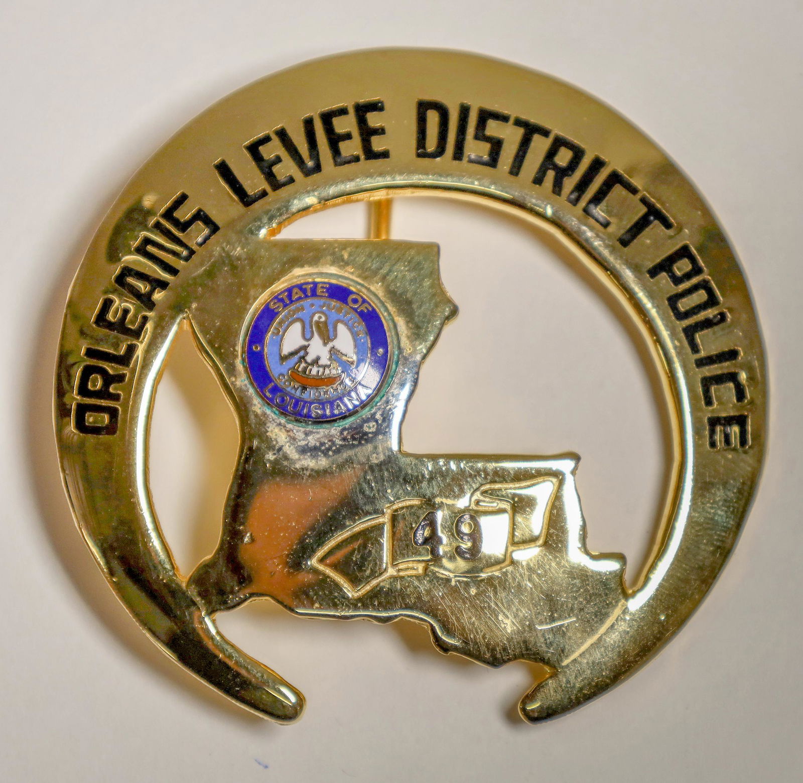 New Orleans Levee District Police Badge [132236]: This is a unique badge with an insert in the shape of the state of Louisiana with the great seal soldered into place. Gold in color and crescent in shape, representing the shape of the City of New Orl