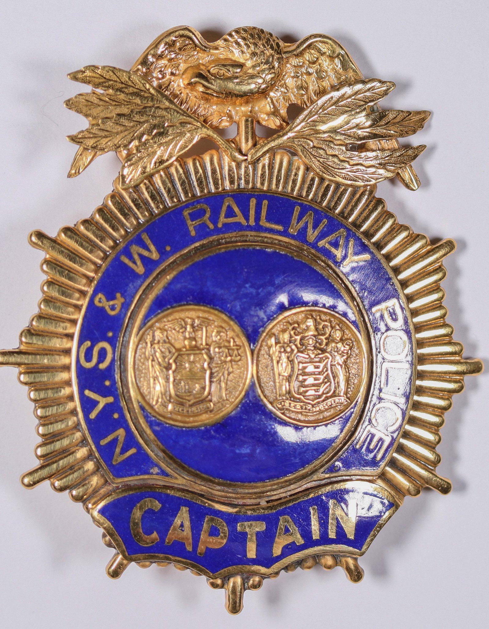 New York, Susquehanna & Western Railway Police Captain: This N.Y.S. & W. Railway Police Captain badge is in a gold tone eagle-top with beautiful blue enamel at 2 3/4 in. tall. It has a single pin-back with rotary clasp. Little to no wear, no hallmark. Date
