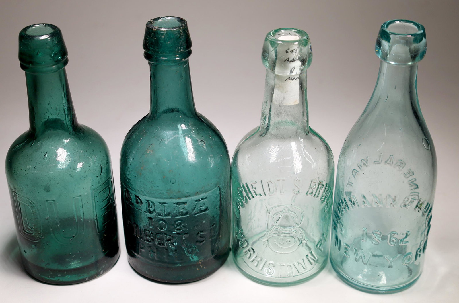 Eastern Soda Bottle Group (4) [132332]: Four Eastern Sodas not listed in Mitchell 2008. 1. "Ed Blee / 108 / Philbert St / Phila" ( In rectangular slug plate) Iron pontil. Green-teal color. Minor surface wear. A couple of glass imperfections