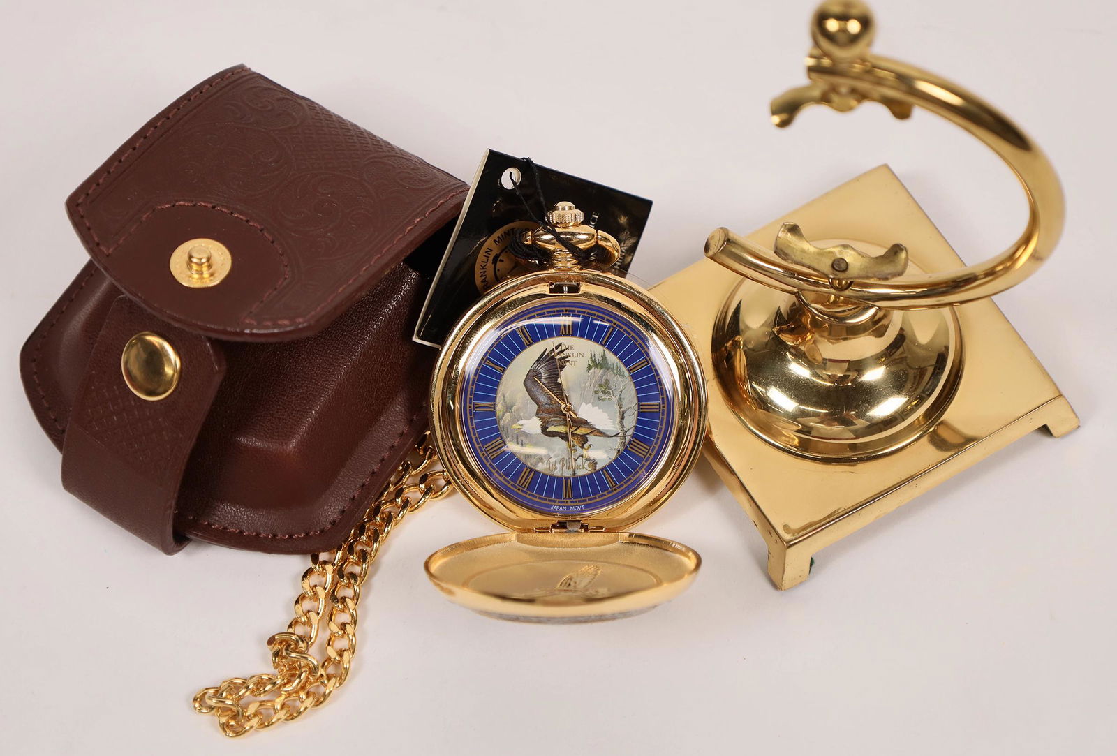 Franklin Mint Eagle Pocket Watch [146370]: This Franklin Mint eagle pocket watch is size 10 movement with display stand. New with FM hang tag, gold tone chain, and leather case. Blue face with roman numerals. Date: Country (if not USA): State: