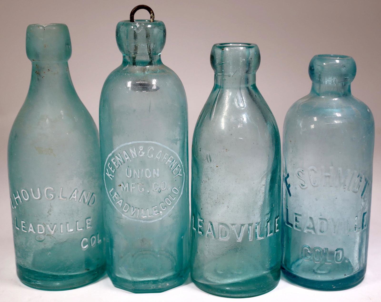 Leadville Bottles, 4 [155944]: 4 Leadville aqua bottles. Blob top embossed Leadville. F. Schmidt/Leadville/Colo. Bruise. Embossed Keenan & Gaffney/ Union Mfg. Co/Leadville, Colo. Lip chip, base bruise, staining. Embossed I. Blob to