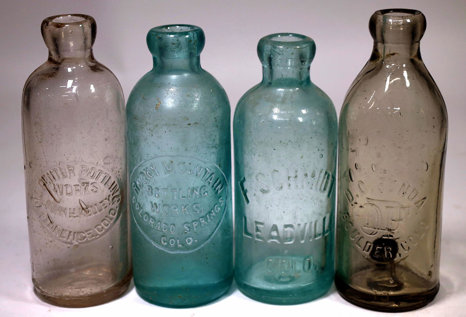 Colorado Soda Bottles, 4 Different [155931]: 4 different Colorado sodas. Embossed aqua Rocky Mountain/ Bottling Works,/Colorado Springs/Colo. Bruises and staining. Aqua F. Schmidt/ Leadville/Colo. Clear, Oil Center Bottling/Works/ John. H. Kelle