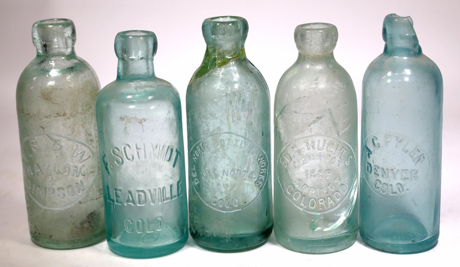 Colorado Damaged Bottles, 5 [155957]: 5 Colorado bottles. Broken lip A.C. Fyler. F. Schmidt/Leadville/Colo. Cracked Ed D. Hughes/Colorado Springs. Cracked/repaired Del Norte Bottling Works. P. S. B. W./Naylon /&/Simpson. Case wear. Date: