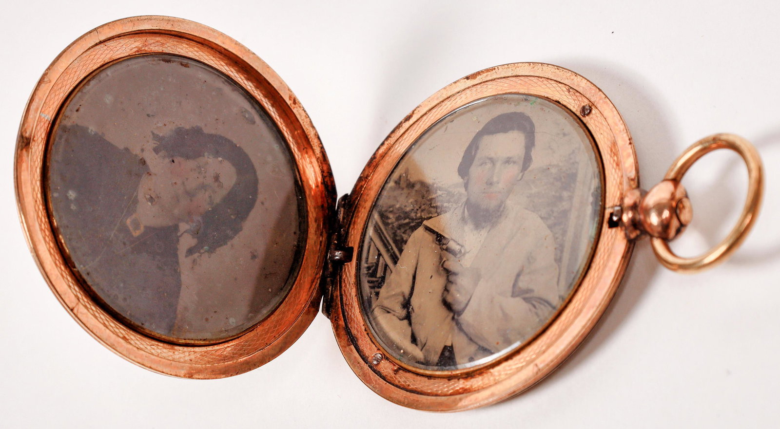 Gold-Plated Locket w/ Tintypes incl. Man with Pistol [163800]: Gold-plated locket with two tintypes of a man and woman, cheeks tinted pink. The man is holding a Model 1849 pocket pistol, the same gun that was very popular with people heading West for the Gold Rus