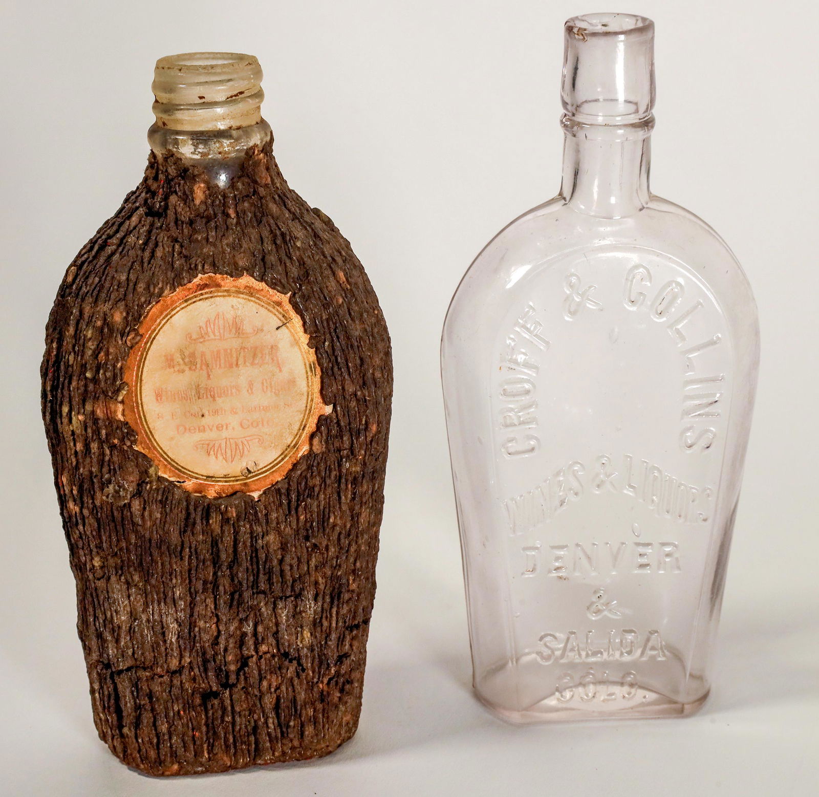 Two Denver Shoo-Fly Flasks [162616]: 1) M Sammitzer Wines Liquors and Cigars. Ground top. Bark covered paper label inserted into glass. Half pint. 2) Croff & Collins wines and liquors. Denver and Salida. Half pint. Air bubble on left sid