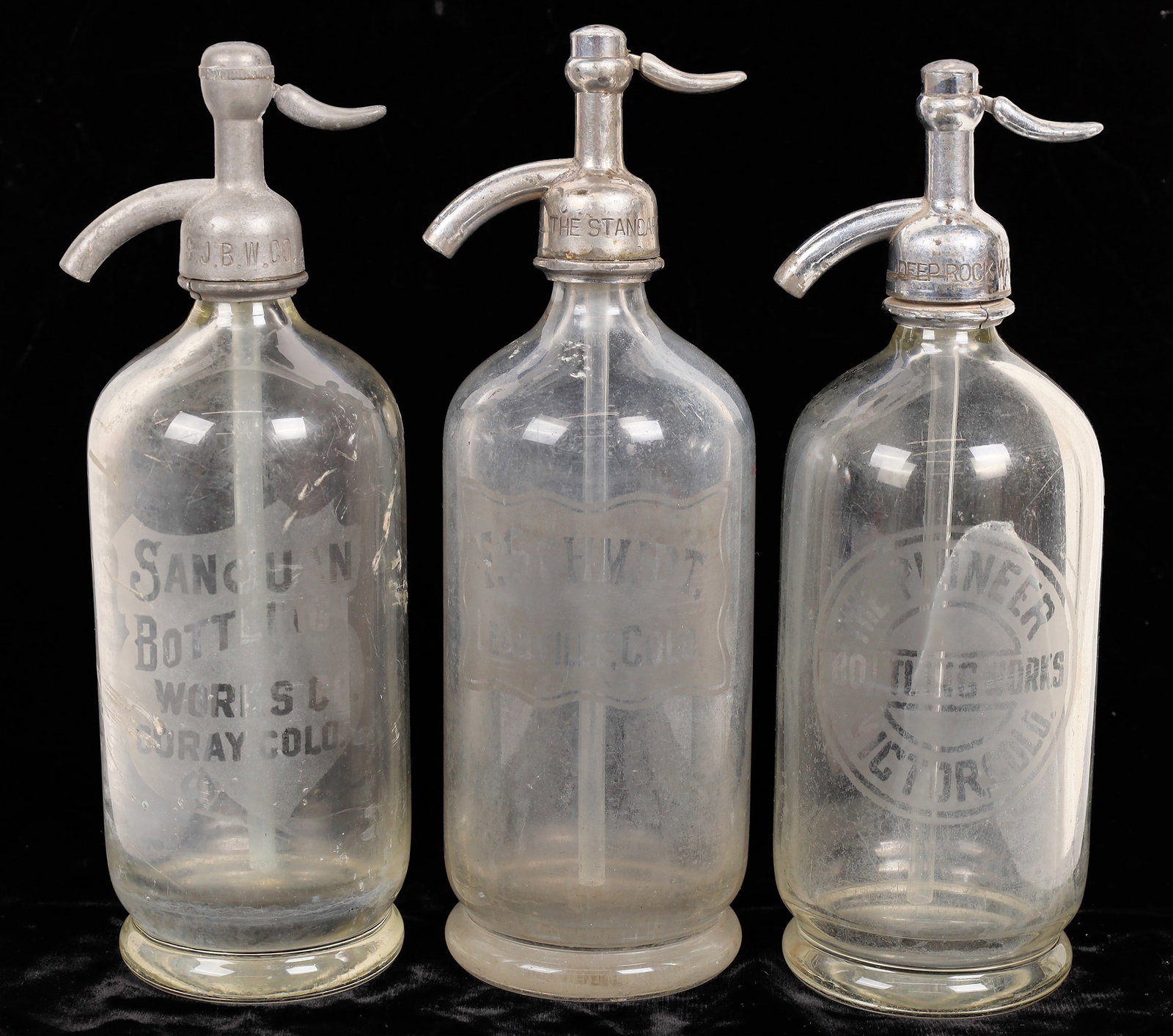 Colorado Mining Camp Seltzer Bottle Trio [168345]: 3 unlisted Colorado mining camp clear seltzer bottles. F Schmidt, Leadville-base ding. The Pioneer Bottling, Victor. San Juan Bottling, Ouray-.3" bruise with small chip on exterior, scratch. Please in