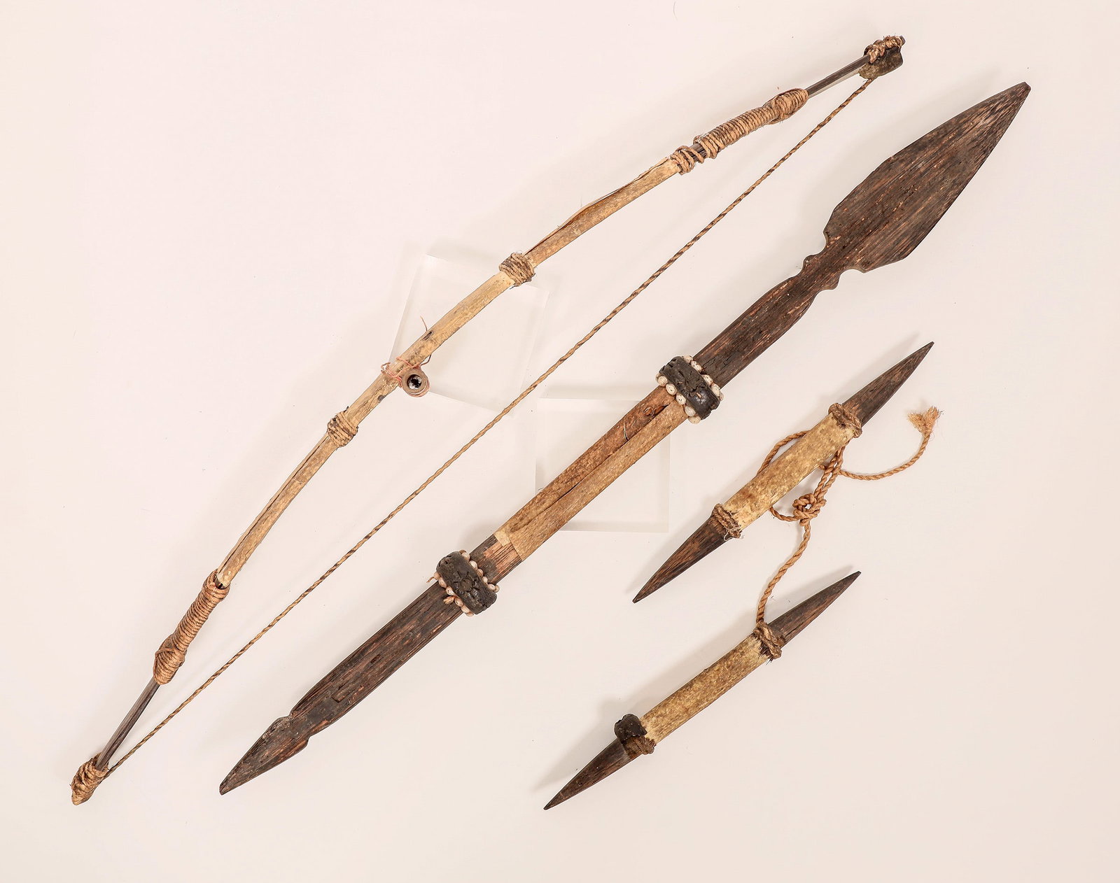 Vintage African Weapons (3) [181044]: A set of three vintage African weapons, includes a bow, two-ended spear and what appears to be pointed nunchucks tied together with jute. All are handmade of wood, leather and jute. Carved leather and