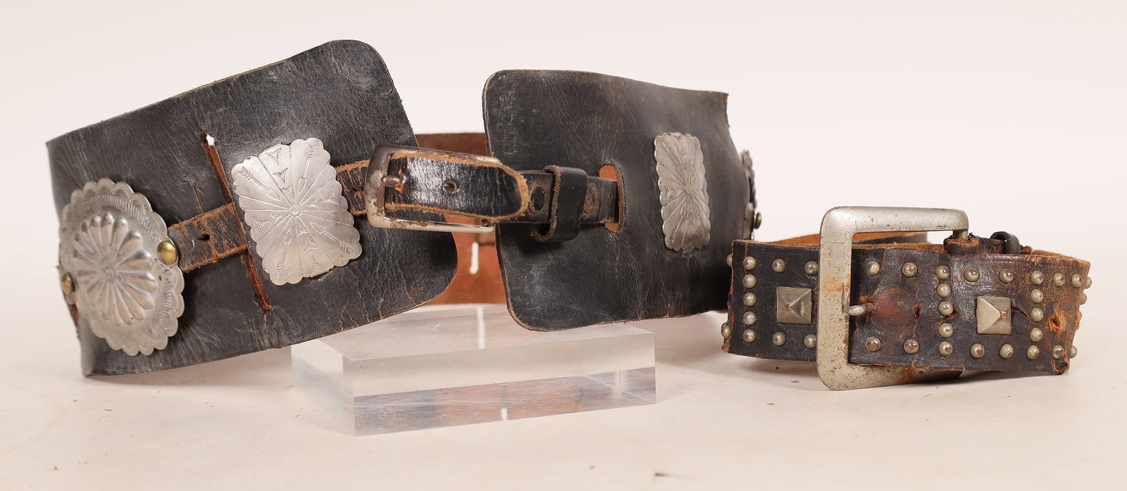 NBC and Fox Prop Leather Belt Pair [178570]: 2 Hollywood props leather belts. Studded belt with points and some jewels removed, 28", stamped NBC prop on back. Size 34 black leather with 7 conchos, stamped FOX PROP on back. [Hollywood] [Californi