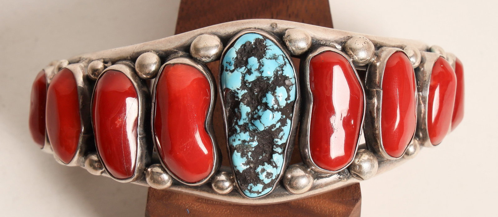 Turquoise and Coral Cuff [162640]: Gallup, N.M.Heavy silver cuff with raw turquoise center stone and 10 graduated in size coral stones. Silver drops on silver cuff. 2.5" inside measure, 1.5" opening. No hallmark. Frank Lewton Collectio