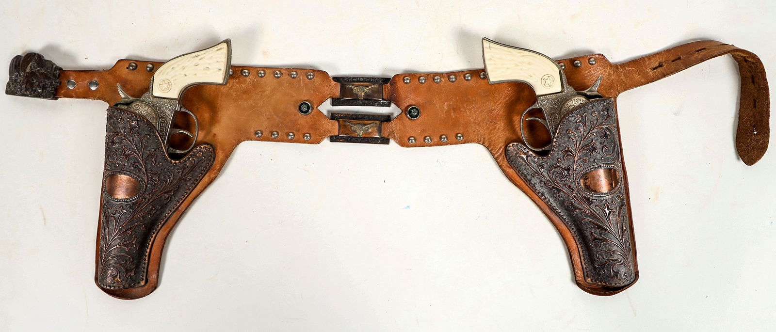 Hubley "Rodeo" Cap Guns with Copper Holsters [196973]: This cap gun set has two Hubley "Rodeo" cap pistols and the holsters are made of copper. Both pistols are not operative. The belt has a very intricate cast metal buckle with a Conestoga wagon scene in