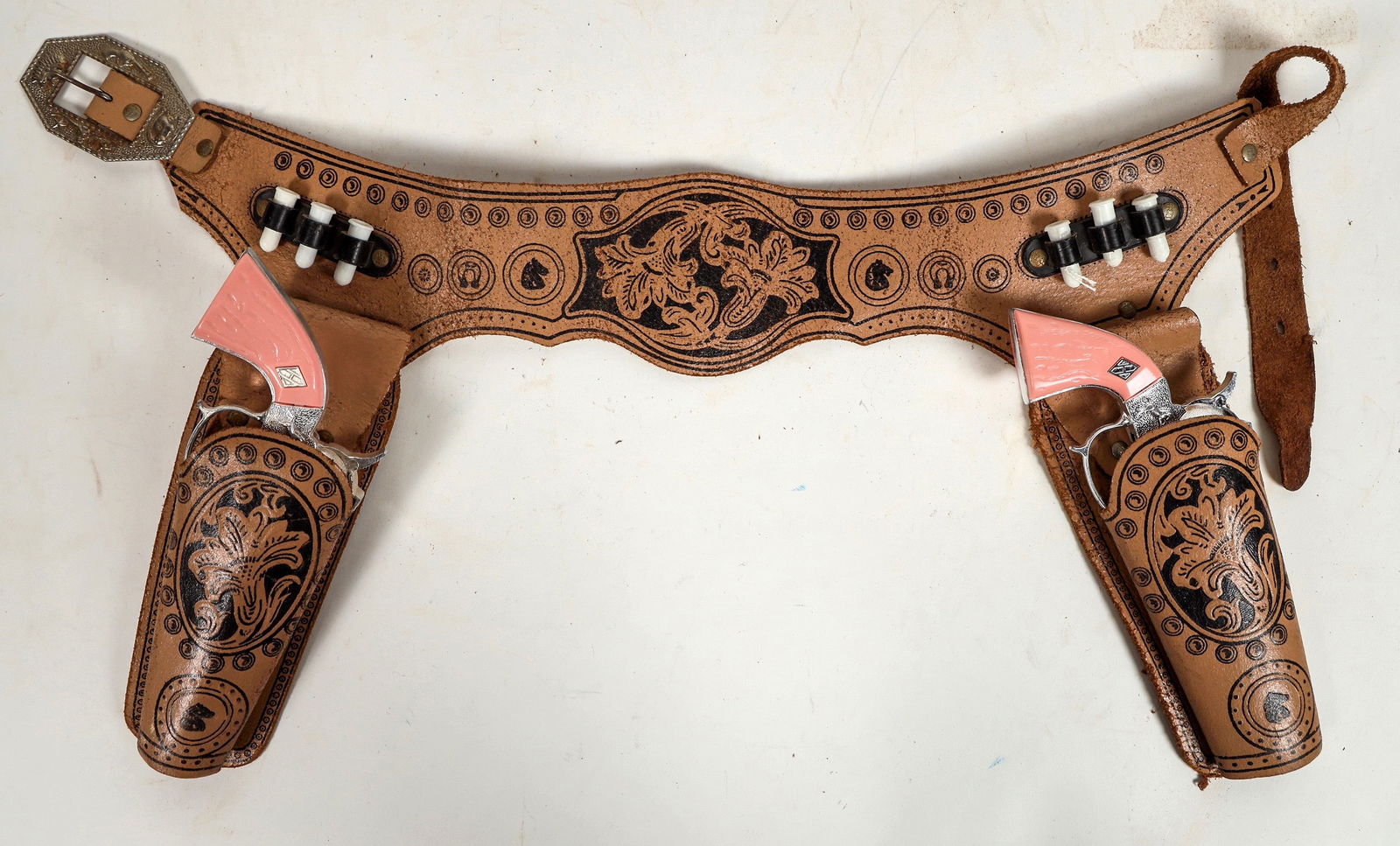 Hubley Cap Pistols with Cowgirl Pink Grips [196978]: This Hubley cap gun rig has two pistols with cowgirl pink grips. The leather holsters and belt are printed pattern tooling with six plastic bullets. Pistols work in single and double action. Please se