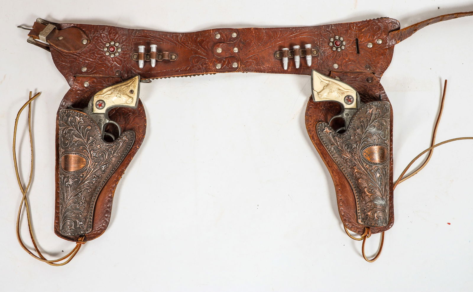 Hubley Cowboy Jr. Cap Guns with Copper Holsters [196979]: This lot has two "Cowboy Jr." pistols with copper holsters on a leather belt . One hammer spur is missing in action. The leather belt holds five bullets. Guns in fair to good condition. Please see pho