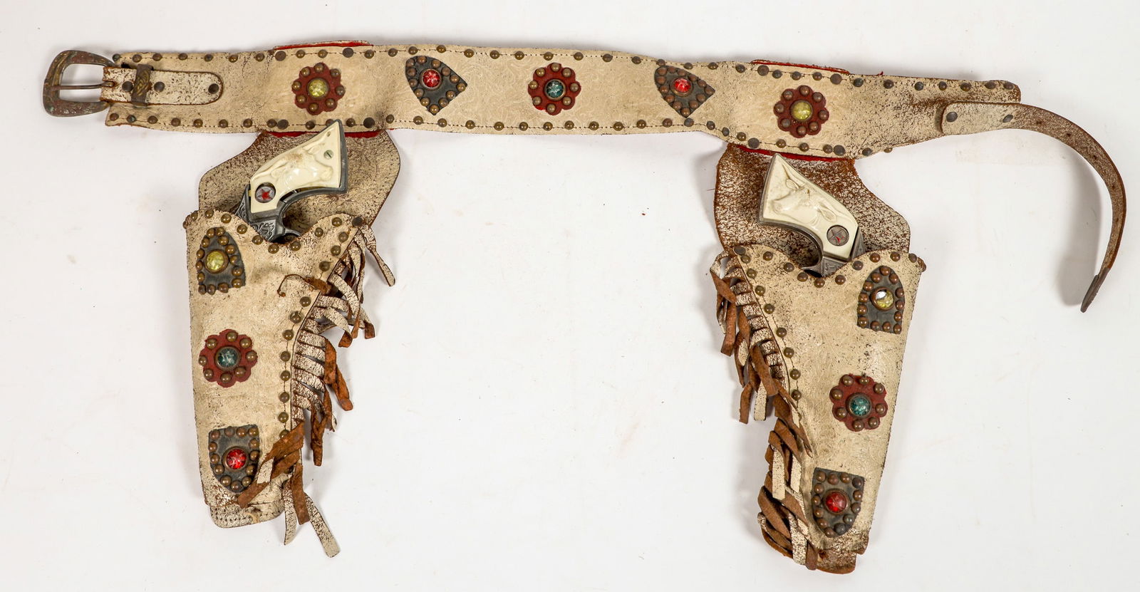 Texas Jr. Two Cap gun with Holsters [196970]: This is a "Texas Jr" two cap gun set with cream colored leather holsters and belt. There are conchos in yellow, green, and red jewels. The guns match with poor fitting plastic grips. One gun works wel