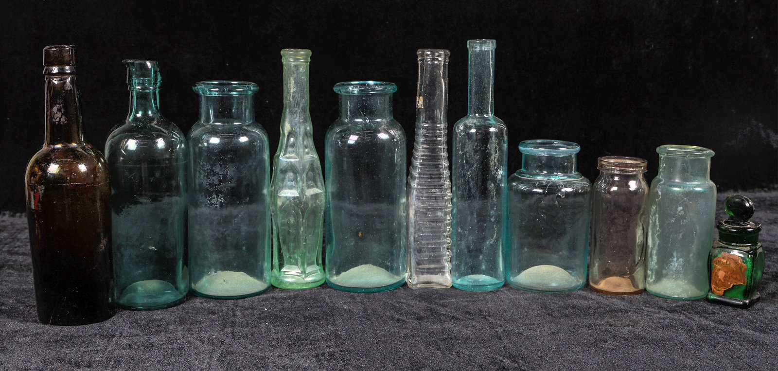 Food Bottle Assortment, 10 [194975]: 10 assorted food bottles, 3.5-8.5". Most interesting one is unmarked aqua open pontil c. 1850's. Also olive dr Sieger, emerald smelling salts with contents, fruits, Pacific and Puget Seattle, pepper s