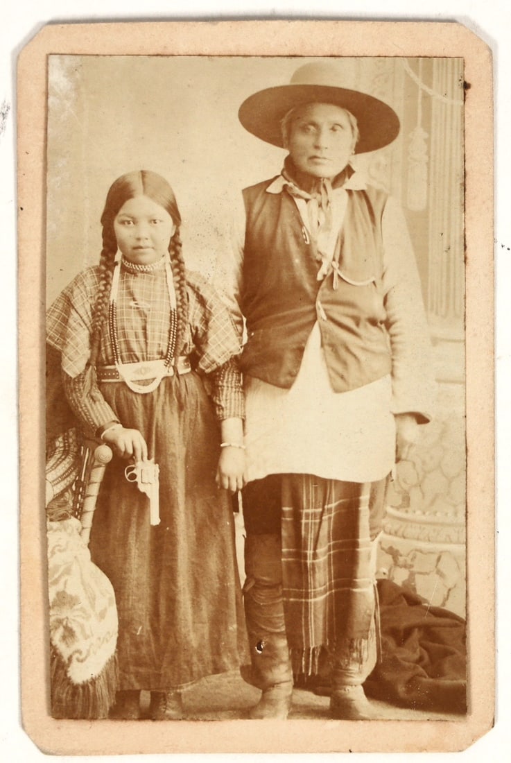 Carte de Visite Photo of Bannack Shoshone with Gun [197235]: This is a CdV photo of a Bannock Shoshone man with a young girl holding a pistol. The revolver is a Hopkins and Allen break-top revolver. Clearly a staged studio photo where the girl holds the gun wit