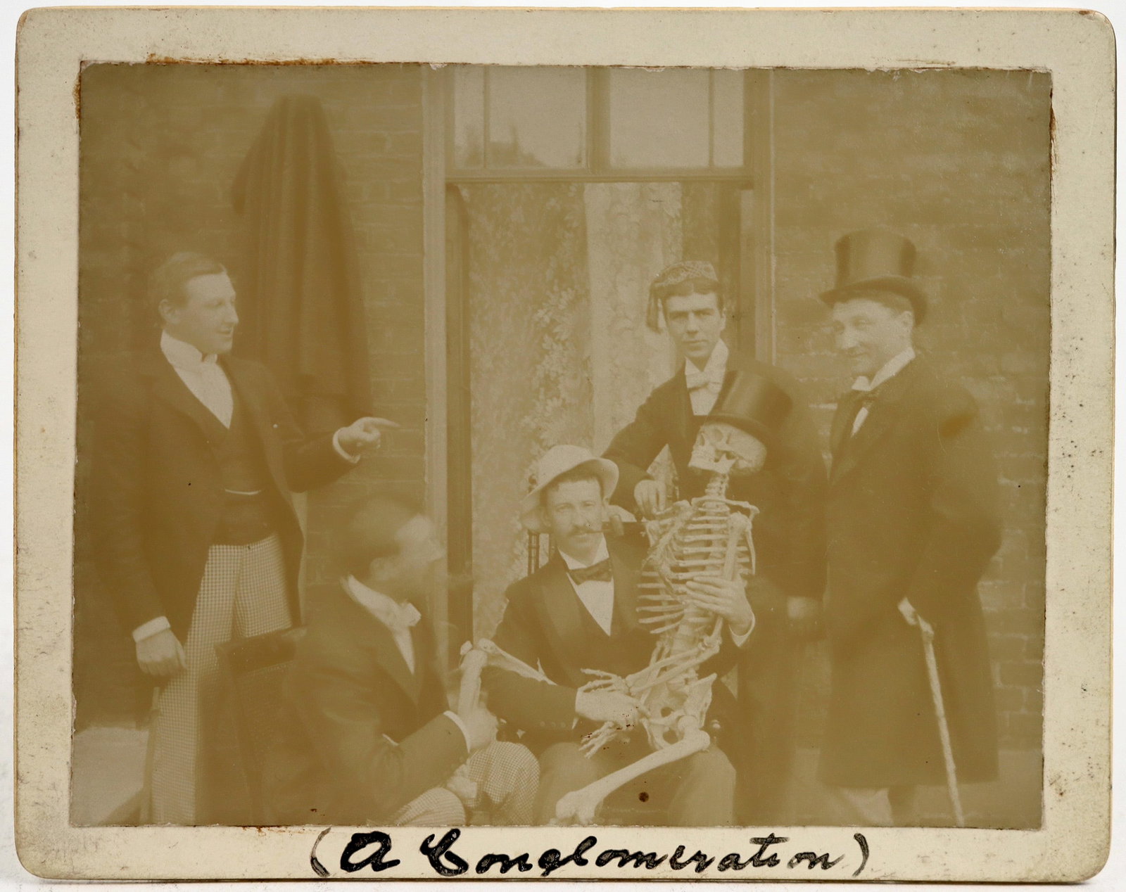 c1885 Silly Med Students w/ Skeleton [200405]: Medical school students posed humorously (pun intended) with a skeleton in lap, wearing hats. Dated c1885, with a self ID stating June 3rd, 1895 on the back. Photo measures 4.3x3.5", on a backing meas