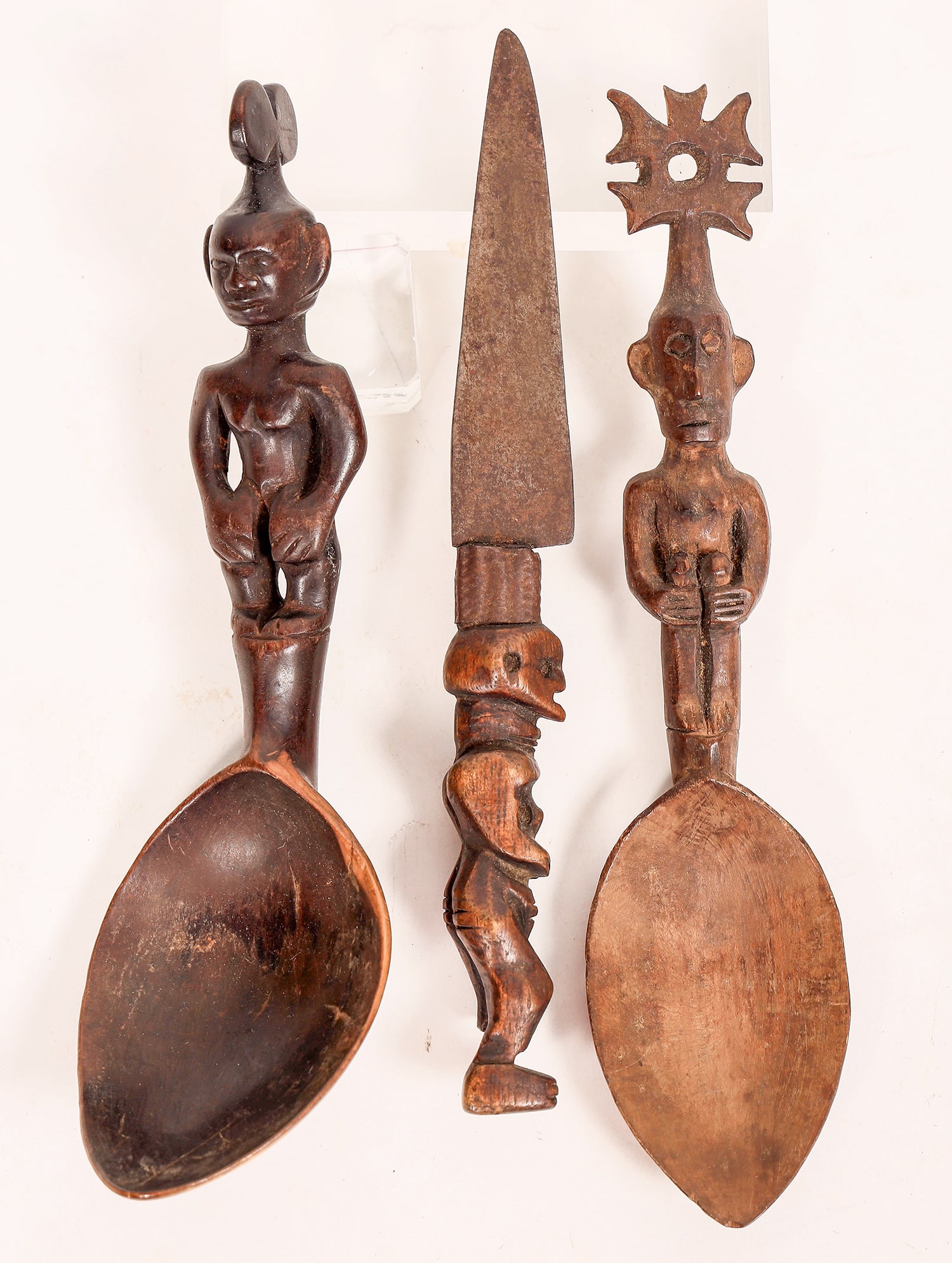 African Hand Carved Utensils c1920s? (3) [181334]: A trio of hand carved wooden utensils from Africa, possibly from the 1920s. Includes two serving spoons with human/native figures as handles, & one knife, with metal blade & skeleton-like figure as th