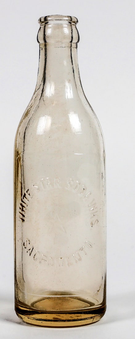 White Star Soda Works Sacramento Soda Bottle [201124]: This lot is a clear ABM soda bottle with a crown cap. The bottle is from the 1920s era and has the words, "White Star Soda Works, Sacramento" boldly embossed on the front, encircling an embossed star.