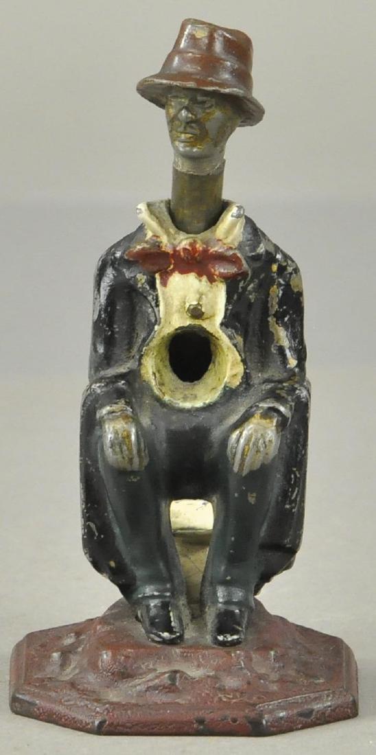 NOVELTY FIGURE CIGAR CUTTER: 985. NOVELTY FIGURE CIGAR CUTTER | Man w/pants down sitting atop a chamber pot. Push on hat to cut cigar, tips fall out of back end into pot. Painted spelter w/great details. Provenance: The Pearlman
