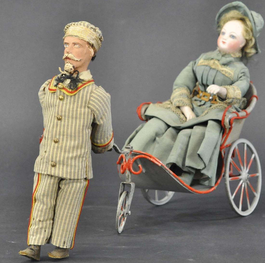 ARISTOCRATIC WOMAN PULLED IN MECHANICAL RICKSHAW: 269. ARISTOCRATIC WOMAN PULLED IN MECHANICAL RICKSHAW | Seated in a painted metal open pull coach with three metal wheels and pulled along by a goateed man in a striped cotton suit, perhaps in a situa