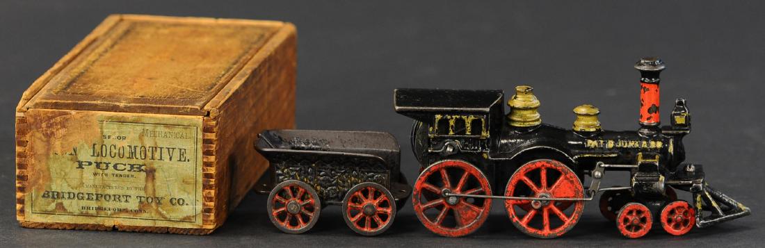 BOXED SECOR "PUCK" LOCOMOTIVE: 778. BOXED SECOR "PUCK" LOCOMOTIVE | Clockwork floor runner, earliest wind-up cast iron locomotive, wind-up mechanism is barely housed by locos cab, tapered boiler and fender over drive wheel is charm