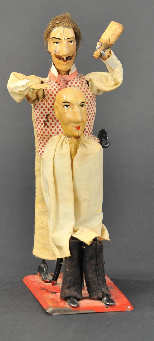 MARTIN THE BARBER: 127. MARTIN THE BARBER | France, c. 1903, hand painted tin, very amusing toy depicts barber attempting to polish bald mans head, clockwork driven. | 8" h.