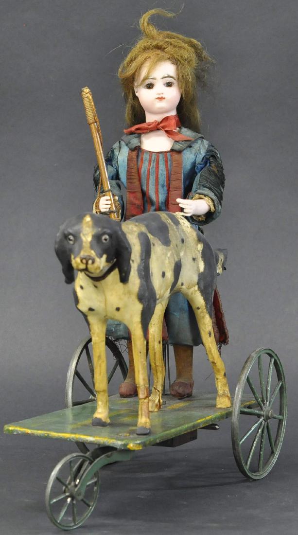 GIRL AND DOG MECHANICAL TOY: 203. GIRL AND DOG MECHANICAL TOY | Larger than average example of young girl, standing with riding crop in right bisque hand and the left resting on the back of her black and white hunting dog compani