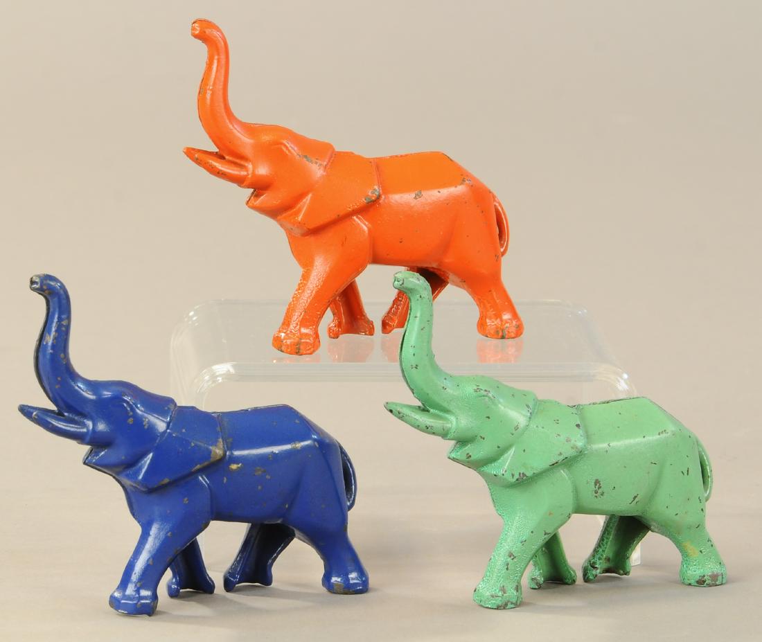 THREE ART DECO ELEPHANT STILL BANKS: 155. THREE ART DECO ELEPHANT STILL BANKS | Cast iron, blue, orange and green painted versions, trunks in air representing good fortune. | 4.5" l. | (Exc.-Pristine Cond.) | $500 - $750