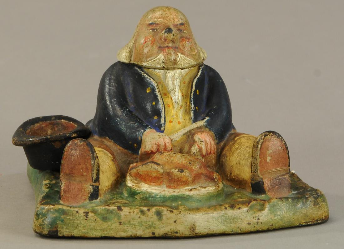 FIGURAL FAT MAN INK WELL: 316. FIGURAL FAT MAN INK WELL | Full figure cast iron mat sits in front of his feast, ink well appears under his hinged head. | (VG - Exc. Cond.) | $300 - $500