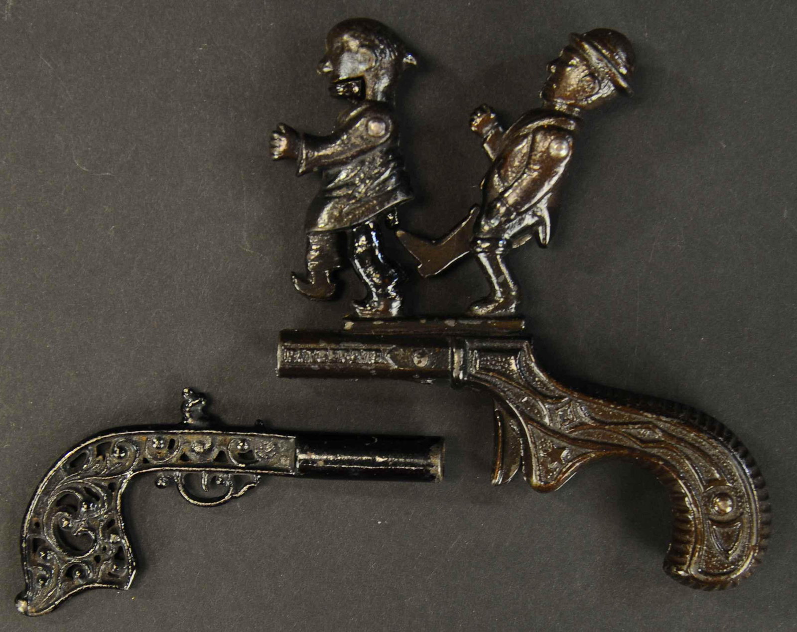 LOT OF TWO CAST IRON CAP GUNS: 316. LOT OF TWO CAST IRON CAP GUNS | circa 1880's, includes a fire cracker gun and Chinese Must Go animated cap gun. | 4.5" - 5.5" length. | Mans leg repaired at gun barrel, jaw possibly replaced. | $