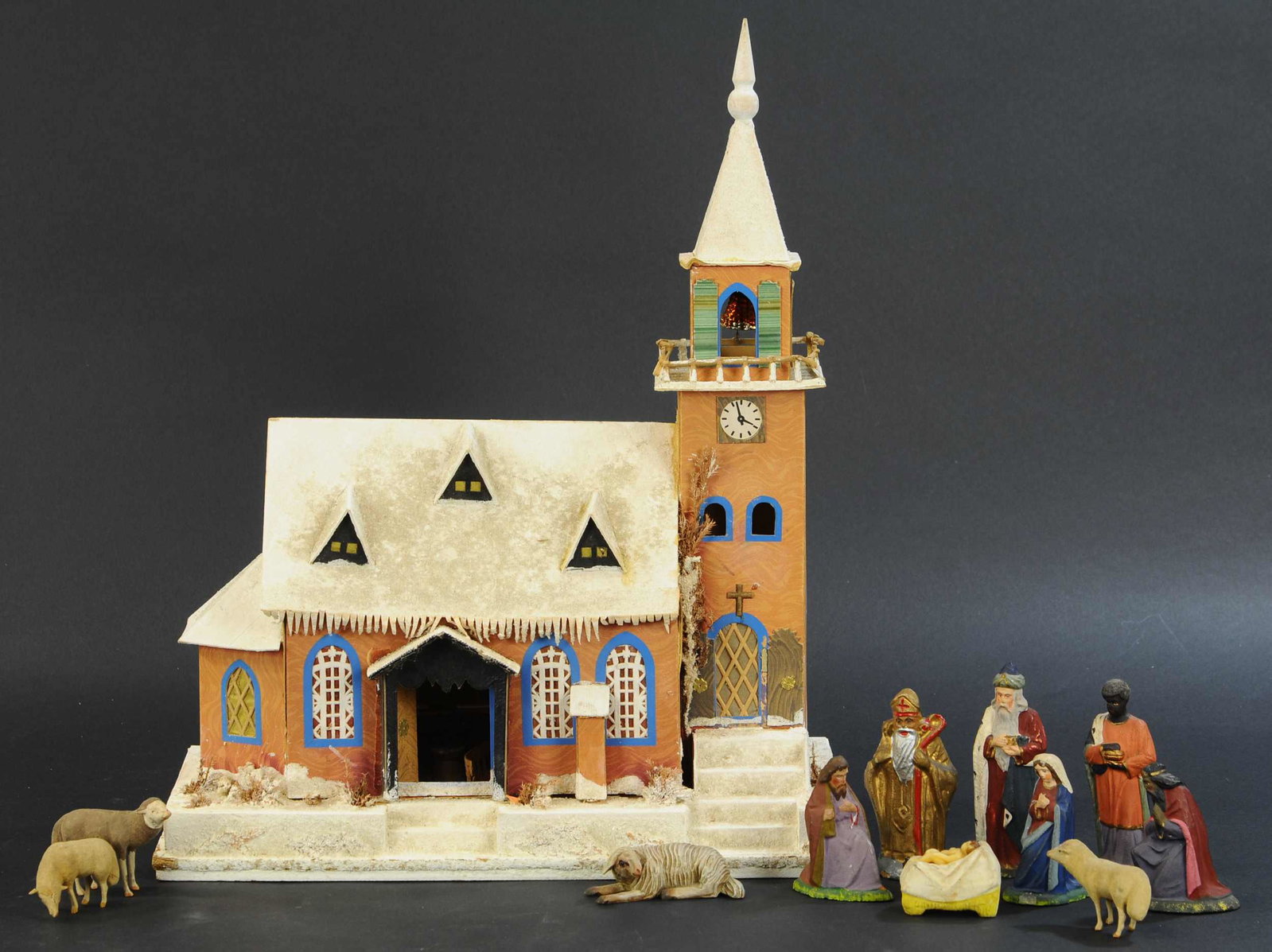 CANDLE-LIT CHURCH WITH CRECHE FIGURES: 520. CANDLE-LIT CHURCH WITH CRECHE FIGURES | Well detailed, pressed cardboard building, crushed glass snow and glass bell in steeple, includes eleven figures. | 18" height. | Has some loose parts, oth