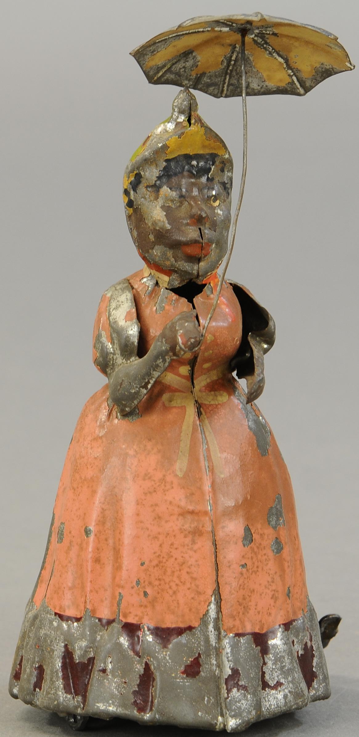 WOMAN WALKING WITH UMBRELLA: 1315. WOMAN WALKING WITH UMBRELLA | Germany, made by Hans Eberl, clockwork strolling action. 8 " | Lead wheels are replaced, otherwise paint in (VG Cond.) | $500 - $750