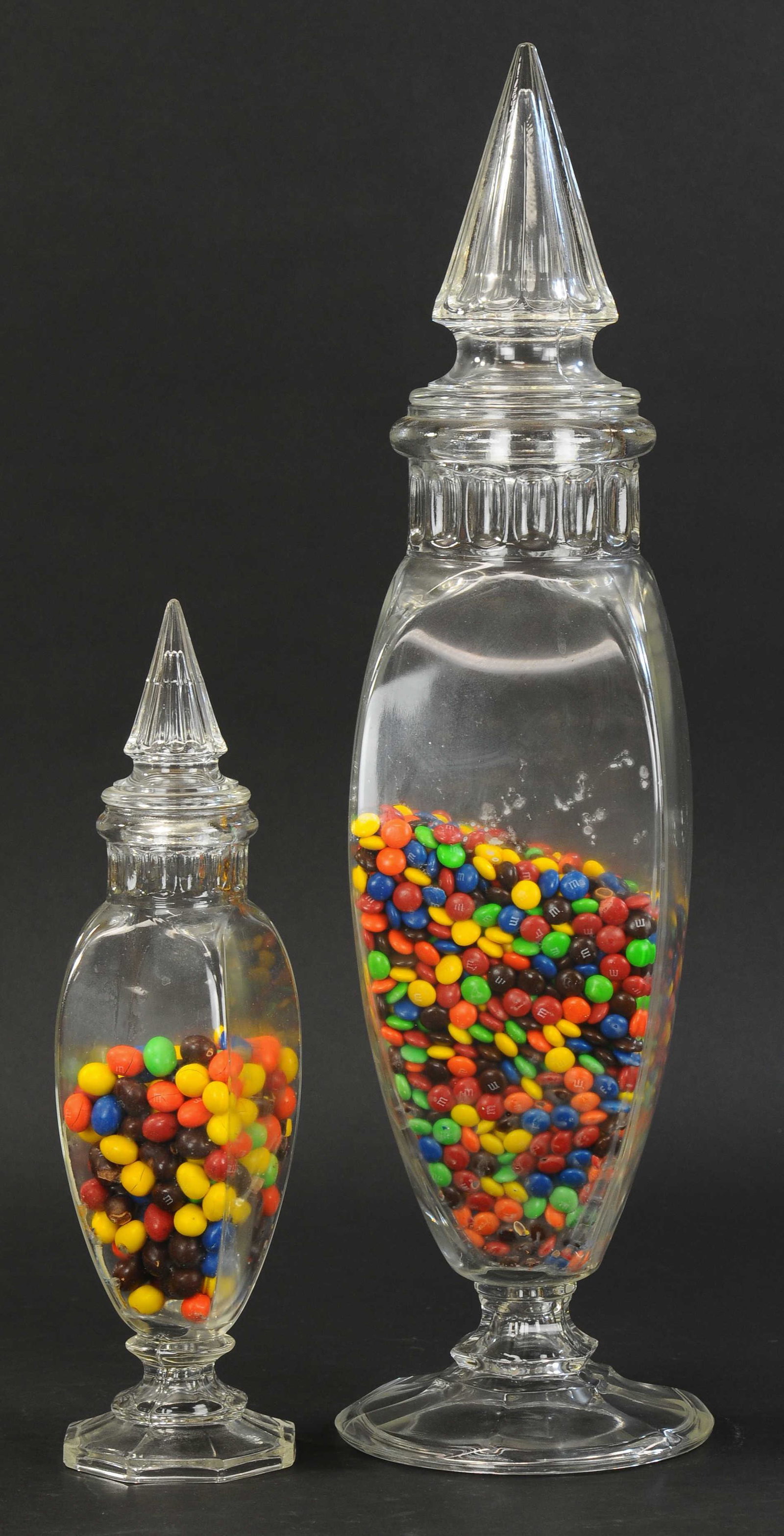 TWO CATHEDRAL TOP CANDY JARS: 2381. TWO CATHEDRAL TOP CANDY JARS | Glass, country store display jars with cathedral tops, a hard to find tall one and companion, smaller one. 16" h. & 26" h. | (Exc. Cond.) | $250 - $500 | Provenanc