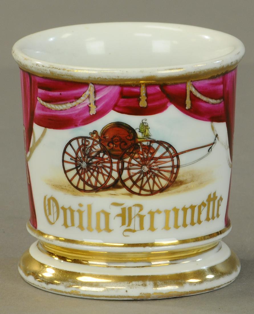 FIREMAN HOSE REEL WAGON SHAVING MUG: 2427. FIREMAN HOSE REEL WAGON SHAVING MUG | Nice use of the drape to add pick up to the illustration. No damage, 30% gold loss. | As Noted. | $200 - $400 | Provenance: Sam Downey Collection.