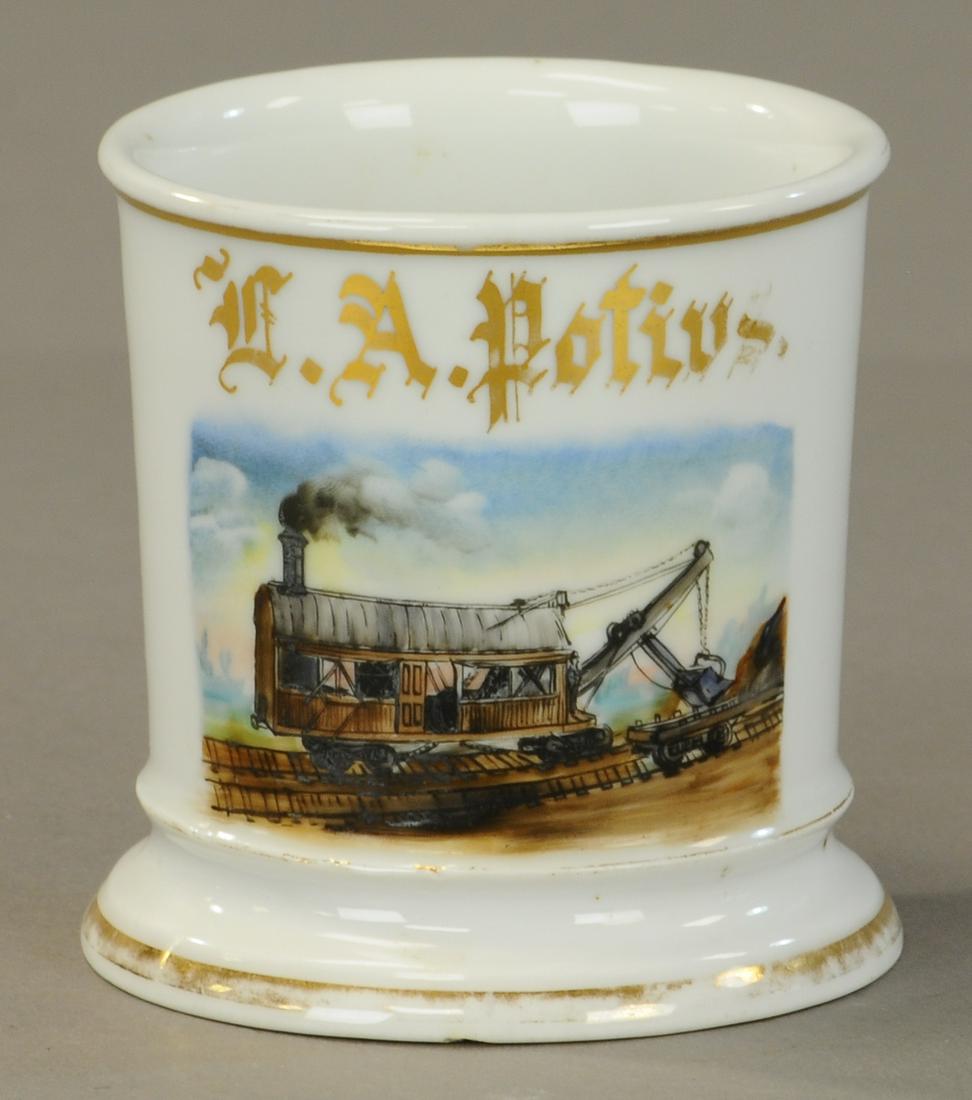 RR STEAM SHOVEL OCCUPATIONAL SHAVING MUG: 2453. RR STEAM SHOVEL OCCUPATIONAL SHAVING MUG | Set on tracks and preforming work. About 30% gold loss slight crack to foot of base. Vary rare - | As Noted. | $800 - $1,500 | Provenance: Sam Downey C