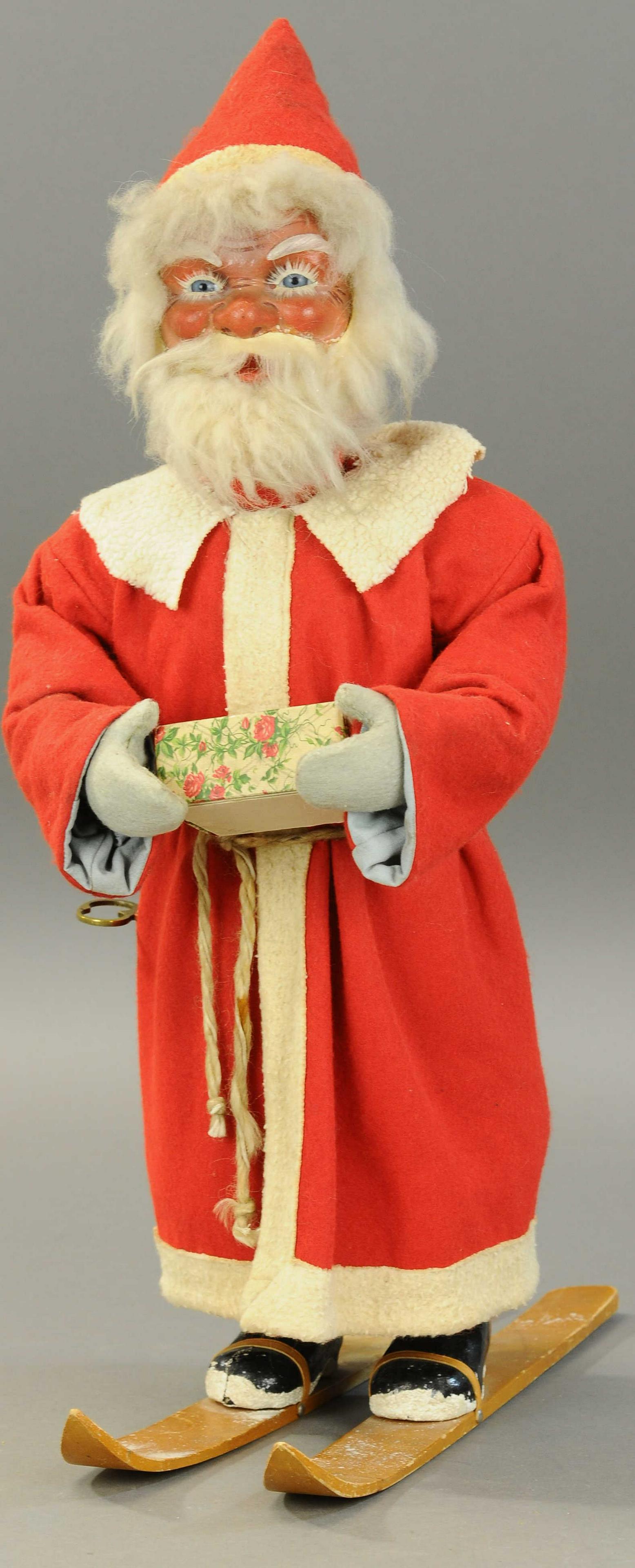 NODDING SANTA CLAUS ON SKIS: 2532. NODDING SANTA CLAUS ON SKIS | Big blue glass eyes and a jolly Santa face of composition w/mohair beard and hair, long red robe w/white trim, leather straps hold his snow tipped boots to the wood