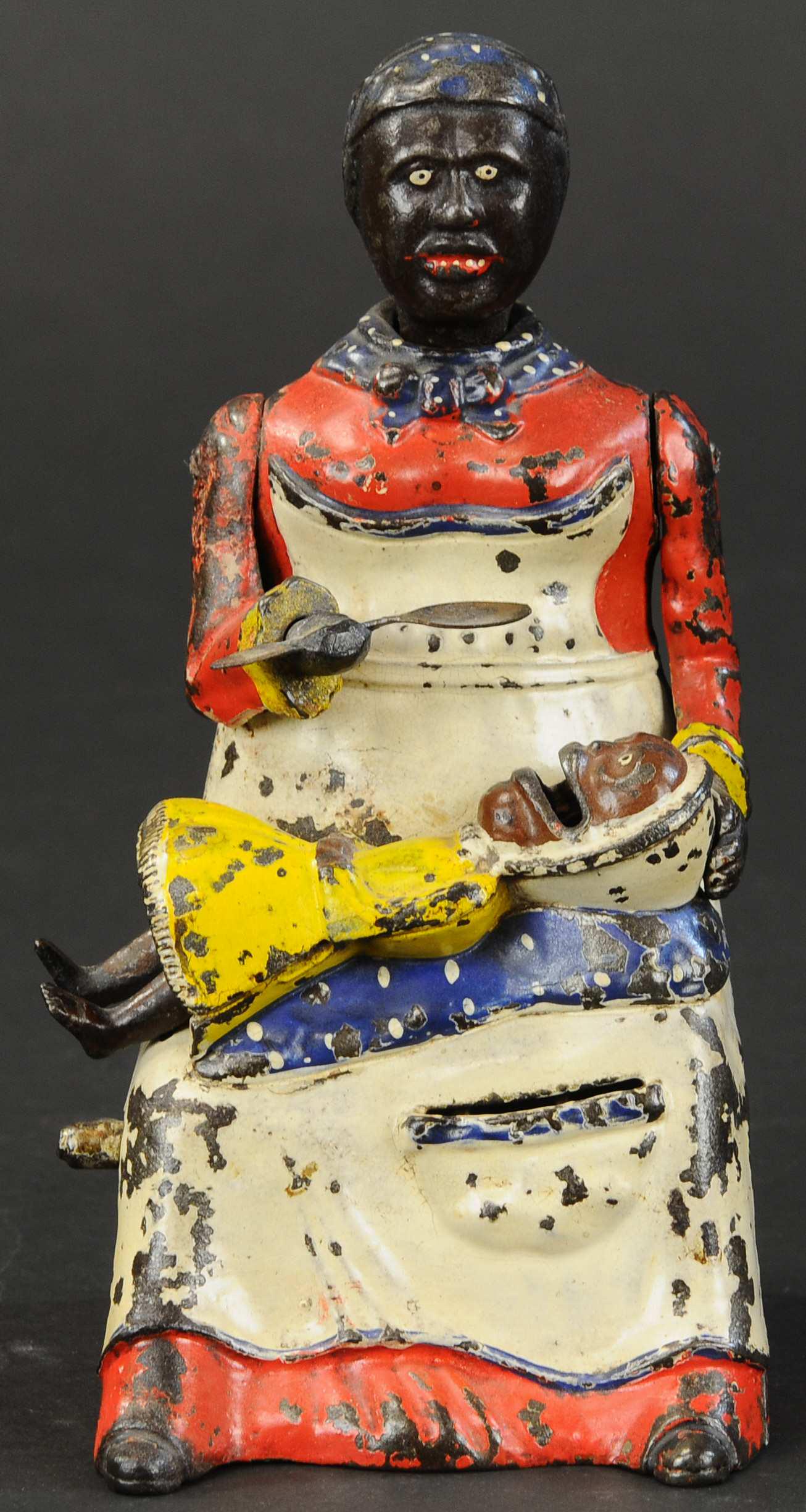 MAMMY W/ SPOON MECHANICAL BANK: 209. MAMMY W/ SPOON MECHANICAL BANK | Kyser & Rex Co., red dress version with yellow dress child, a classic bank. | Enhancement to reds on Mammys right side, spoon reattached, otherwise in (Very Good 