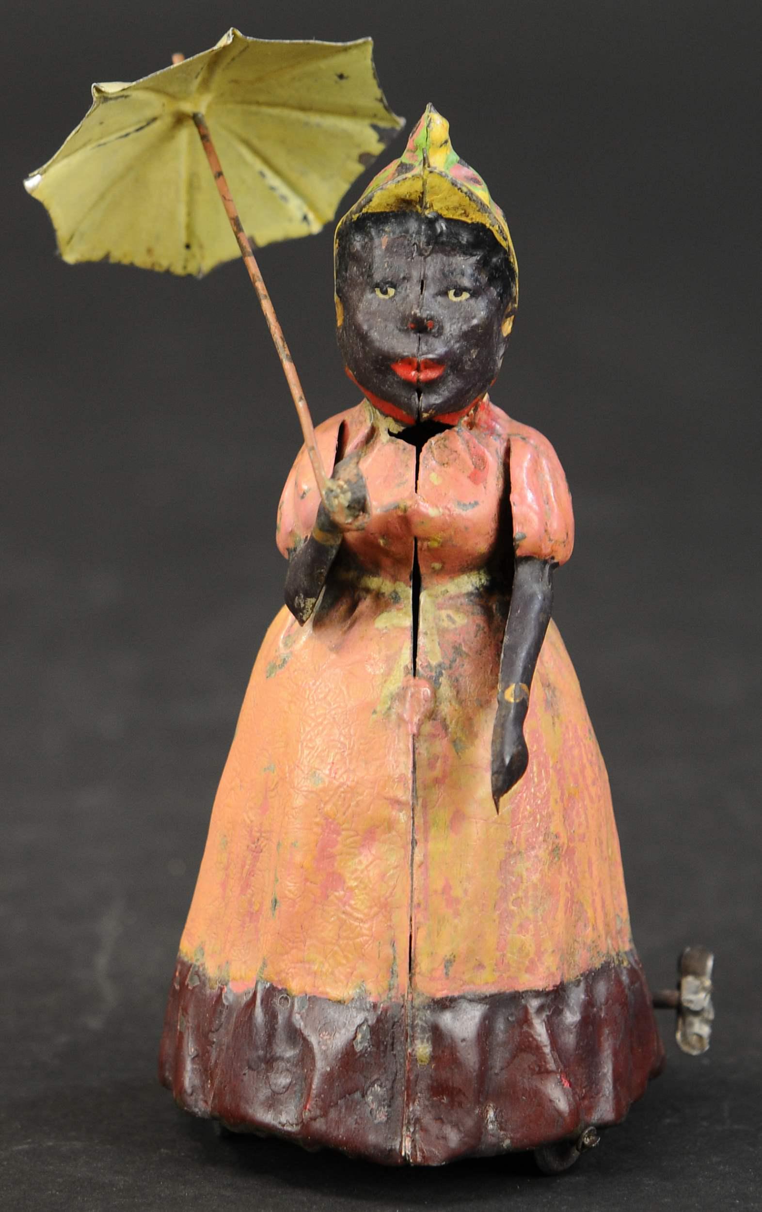 HANS EBERL WOMAN W/ UMBRELLA: 1428. HANS EBERL WOMAN W/ UMBRELLA | A scarce German toy with large shelf presence. | 8" h. | Restored and aged with working bellows. | $500 - $750
