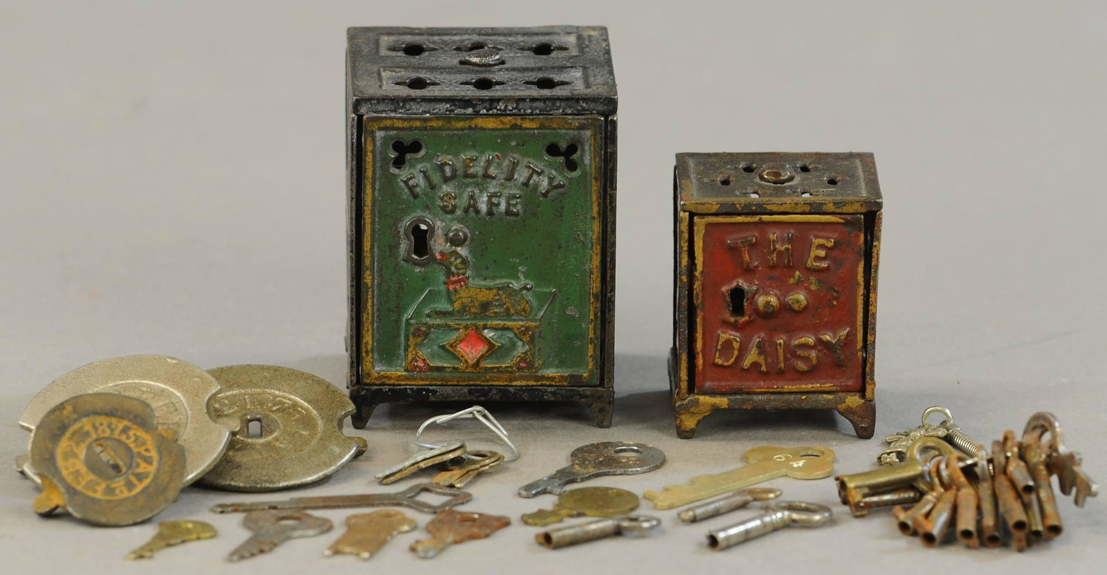FIDELITY & DAISY SAFE STILL BANKS: 77. FIDELITY & DAISY SAFE STILL BANKS | With traps, keys and extra bank parts. | 2" - 3" h. | (VG - Exc. Cond.) | $200 - $400