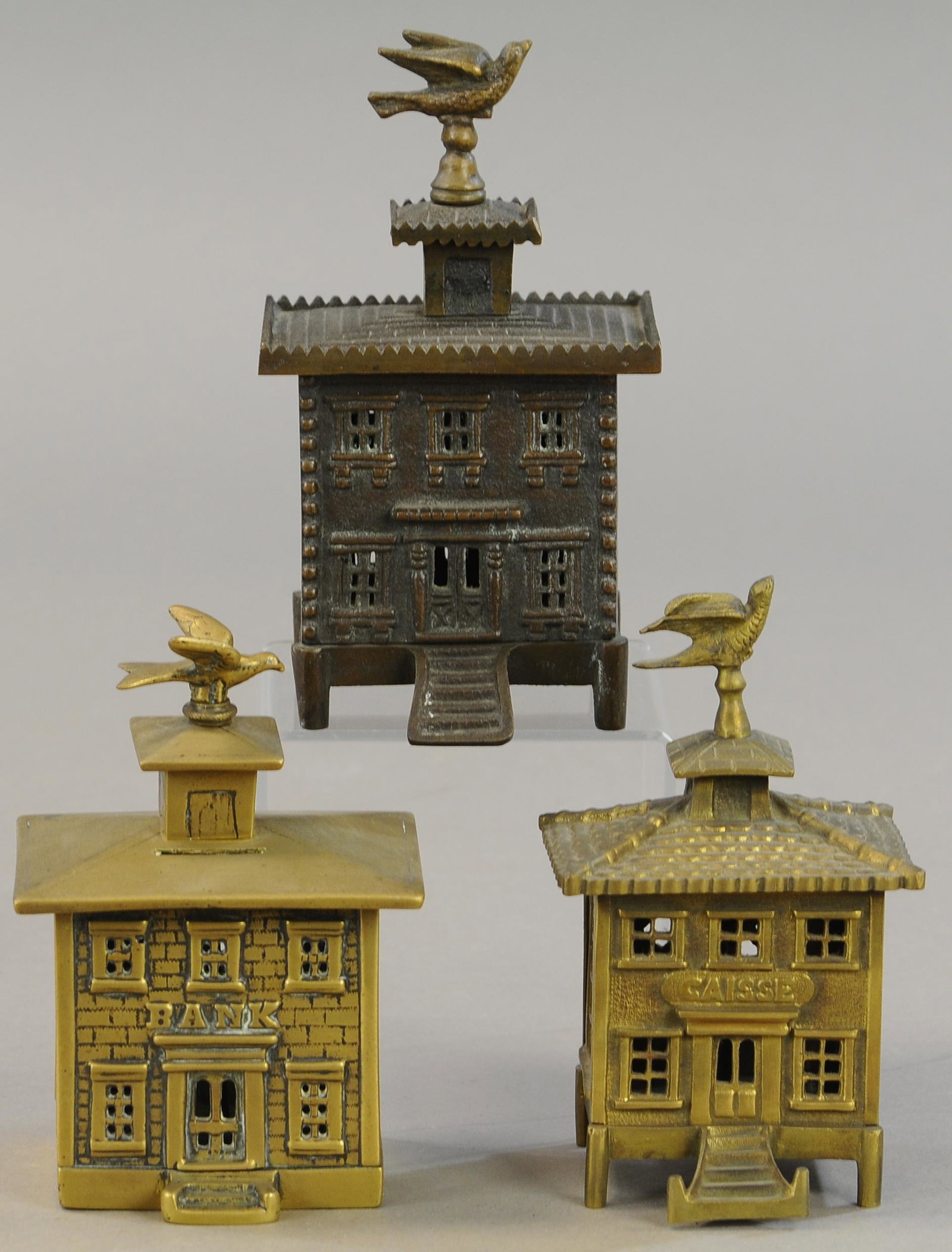 THREE BUILDING W/ BIRD FINIAL STILL BANKS: 163. THREE BUILDING W/ BIRD FINIAL STILL BANKS | Two smaller banks are brass. | 6" - 7" h. | Overall in (Exc. Cond.) | $200 - $400