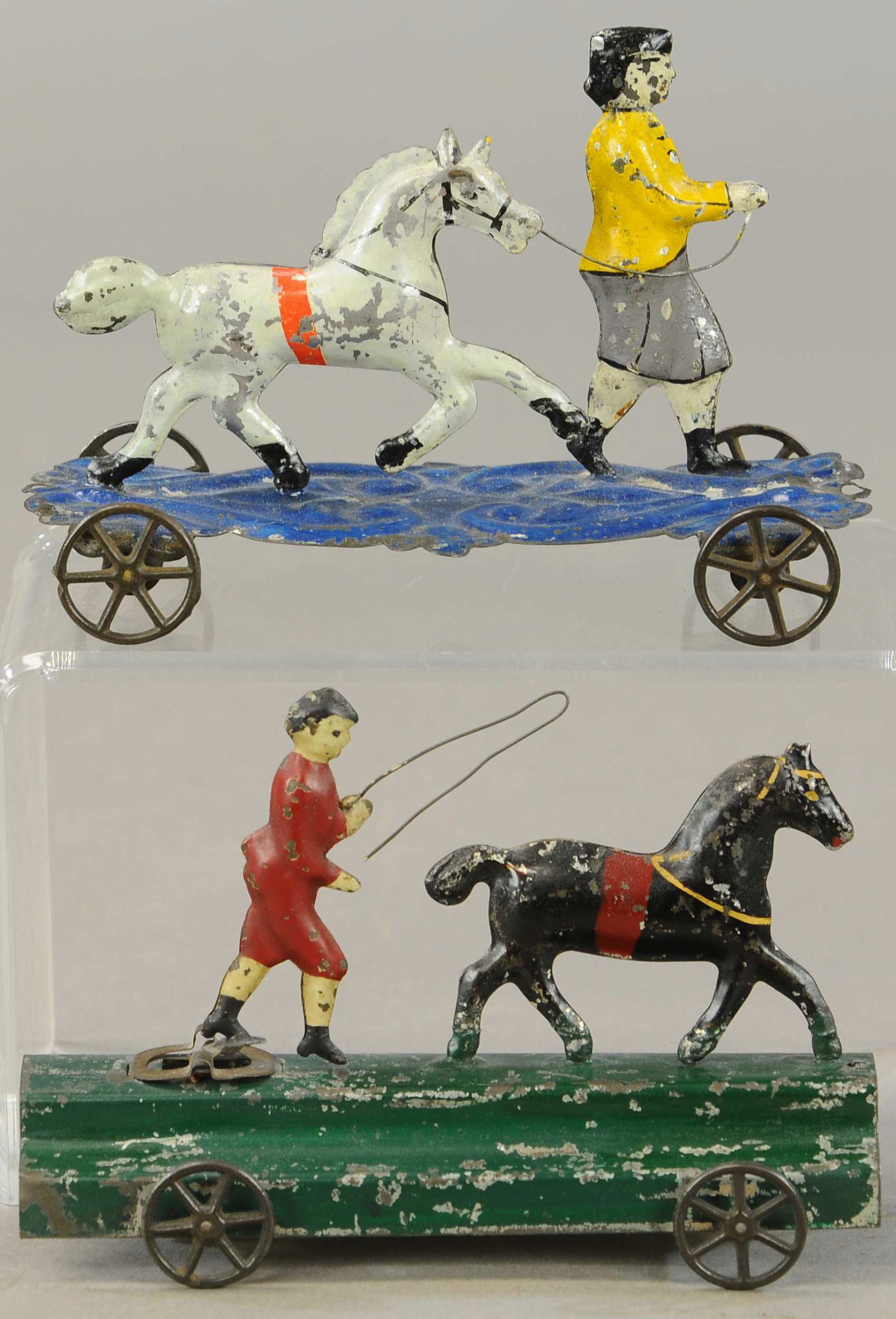 TWO EARLY AMERICAN PLATFORM HORSE TOYS: 222. TWO EARLY AMERICAN PLATFORM HORSE TOYS | 6.5" l. | White horses tail is reattached and repainted, both boys are repainted with some touch-ups throughout both toys. | $200 - $400