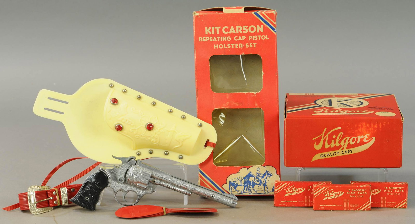 KILGORE KIT CARSON GUN & HOLSTER: 243. KILGORE KIT CARSON GUN & HOLSTER | Lot includes box of 4 doz caps. | 10" l. | Cellophane on box distressed, otherwise in All Original Condition. | $150 - $300