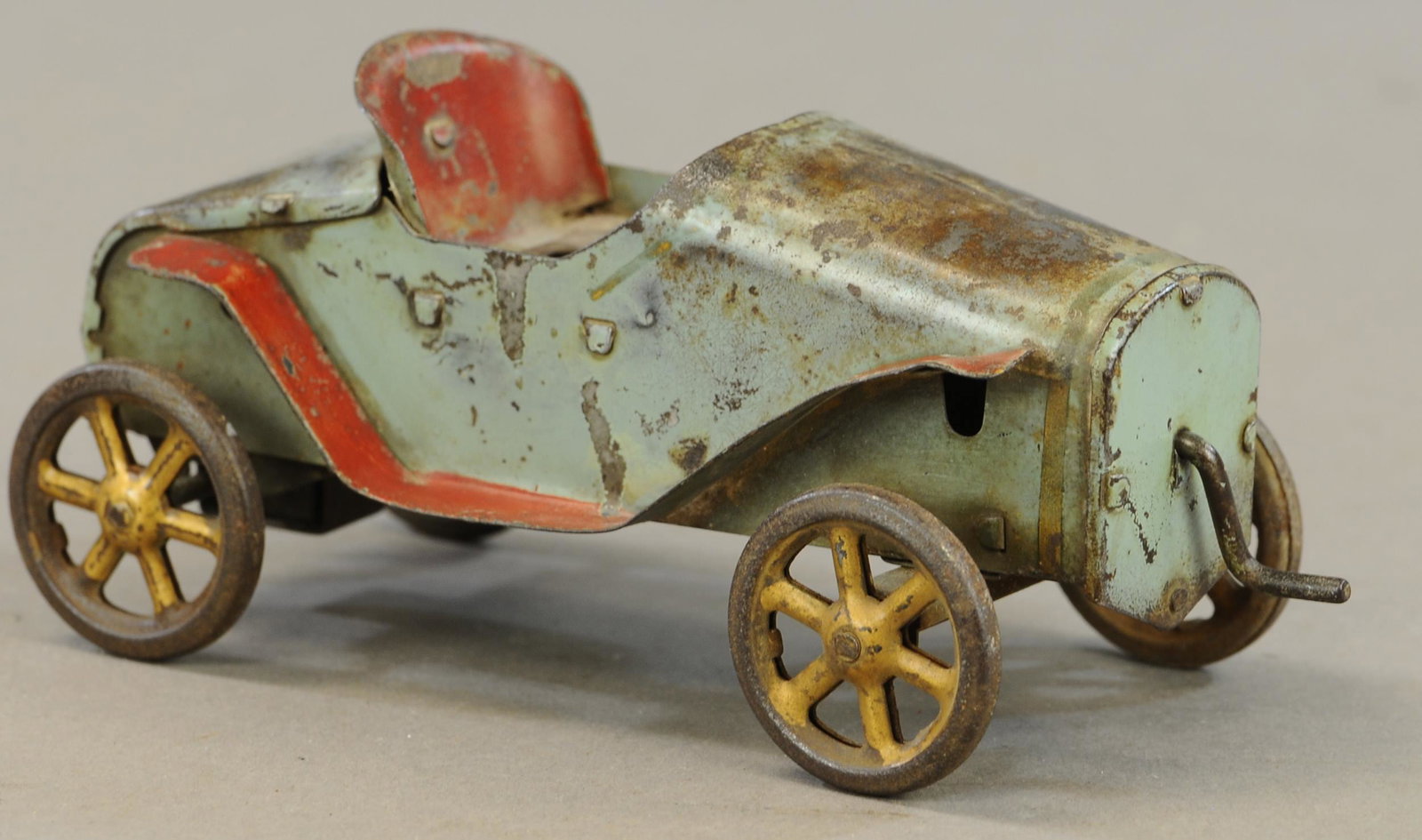 SMALL FRONT CRANK FRICTION RACER: 596. SMALL FRONT CRANK FRICTION RACER | 8" l. | Missing steering wheel and figure, paint in All Original Condition. | $125 - $250