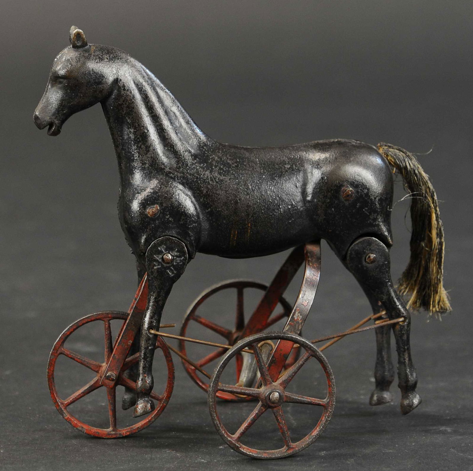 IVES ARTICULATED HORSE ON WHEELS: 30. IVES ARTICULATED HORSE ON WHEELS | As the toy is rolled, the horse's legs seemingly walk which provides a nice visual. | 8" h. | One rear wheel has a small crack at spoke, overall in (Excellent Co