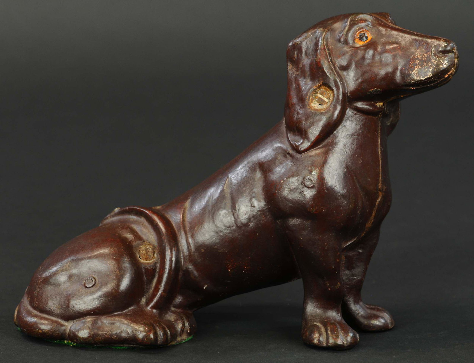 SITTING DASCHUND DOORSTOP: 321. SITTING DASCHUND DOORSTOP | Full figure dachshund in sitting position with tail wrapped around front of body, unusual piece, later casting. | 12" l. | (Excellent Condition) | $600 - $800