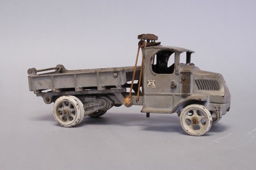 ARCADE MACK DUMP TRUCK: Cast iron, painted in grey overall, ''T'' bar on back of cab for unloading, opening tailgate, seated driver, Mack logo on door and front, white painted spoke wheels, dual on rear. 12'' long.